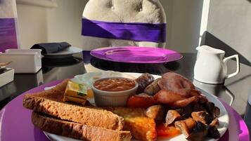 A breakfast plate with toast, beans, bacon, sausages, and eggs on a table.