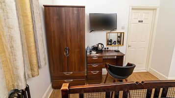 A bedroom with a wooden wardrobe, a desk with a mirror, a television, and a bed with a headboard.