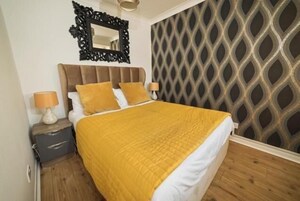 A bedroom with a bed, a nightstand, a lamp, a mirror, and a patterned wall.
