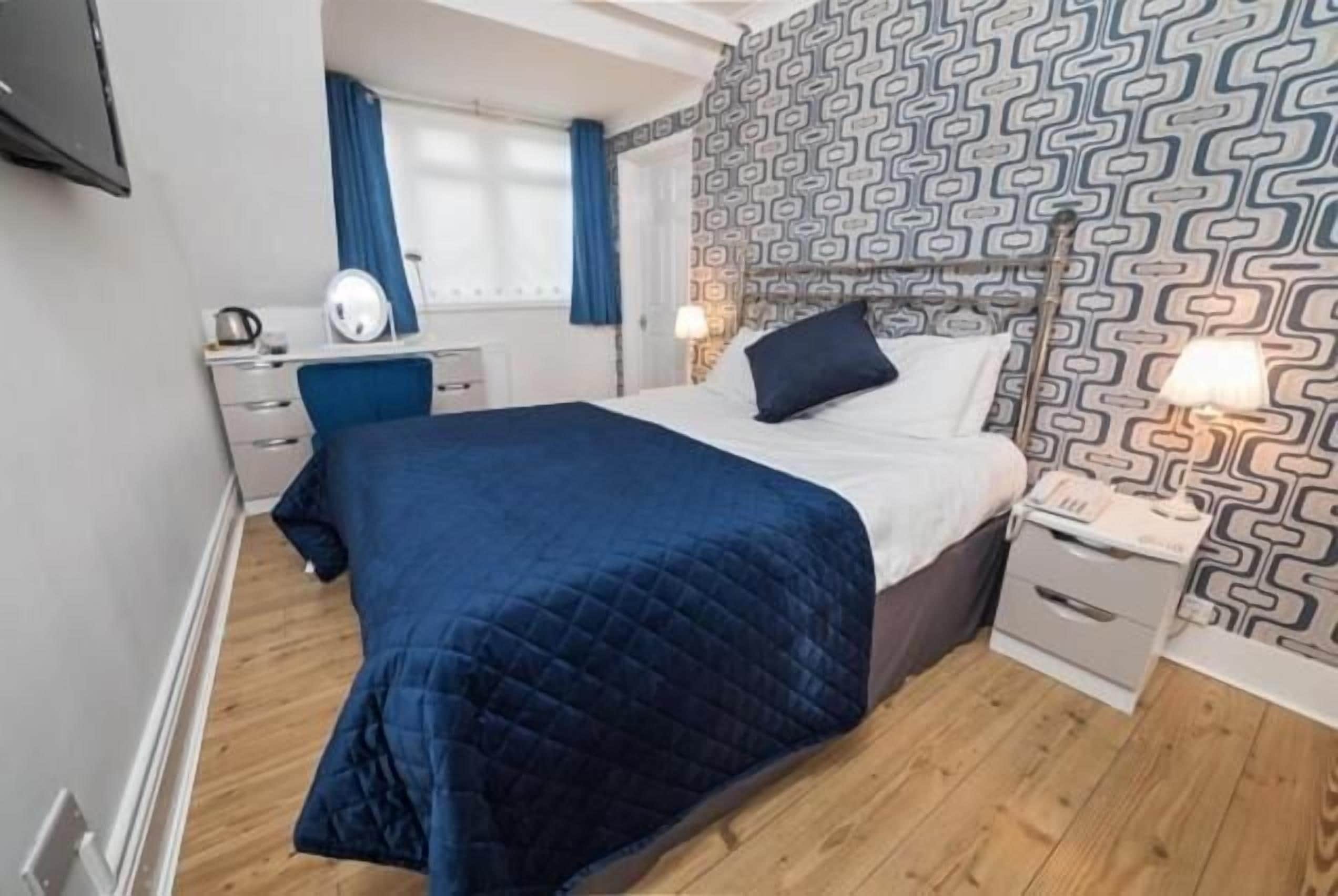 Quarto com cama, mesas de cabeceira, escrivaninha e parede estampada.