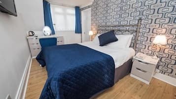 Quarto com cama, mesas de cabeceira, escrivaninha e parede estampada.
