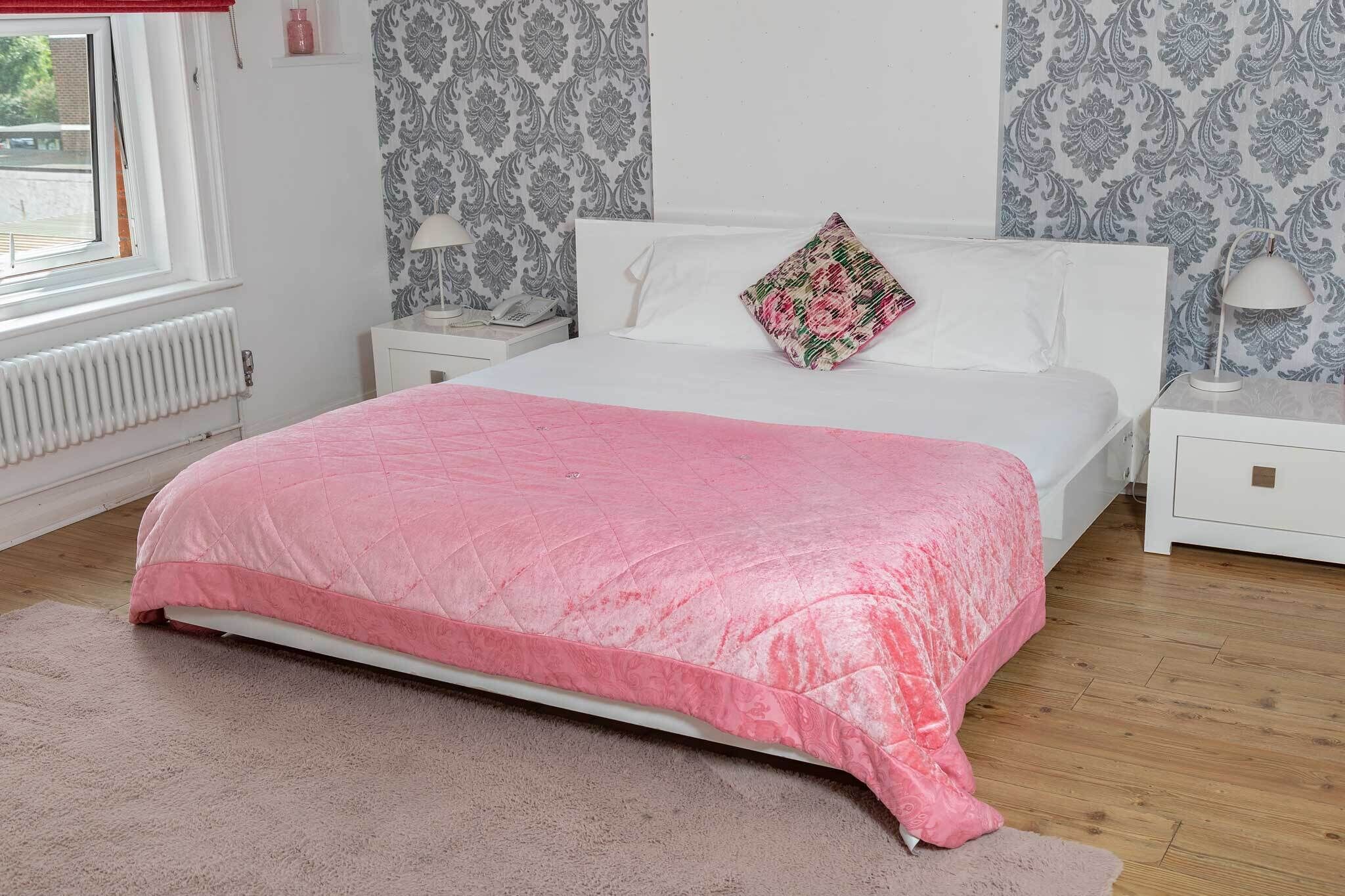 Een slaapkamer met een bed, een nachtkastje, een lamp, een radiator en behang met een patroon.