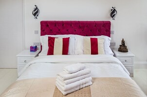 Una cama bien tendida con cabecera roja, ropa de cama blanca y una pila de toallas blancas al pie.
