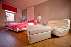 A bedroom with a bed, a bedside table, a lamp, a chair, and a window.
