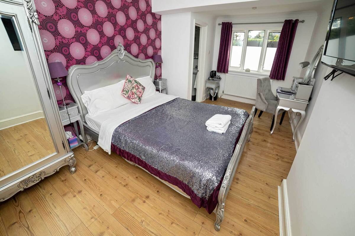 A bedroom with a large bed, a desk, a chair, and a mirror.