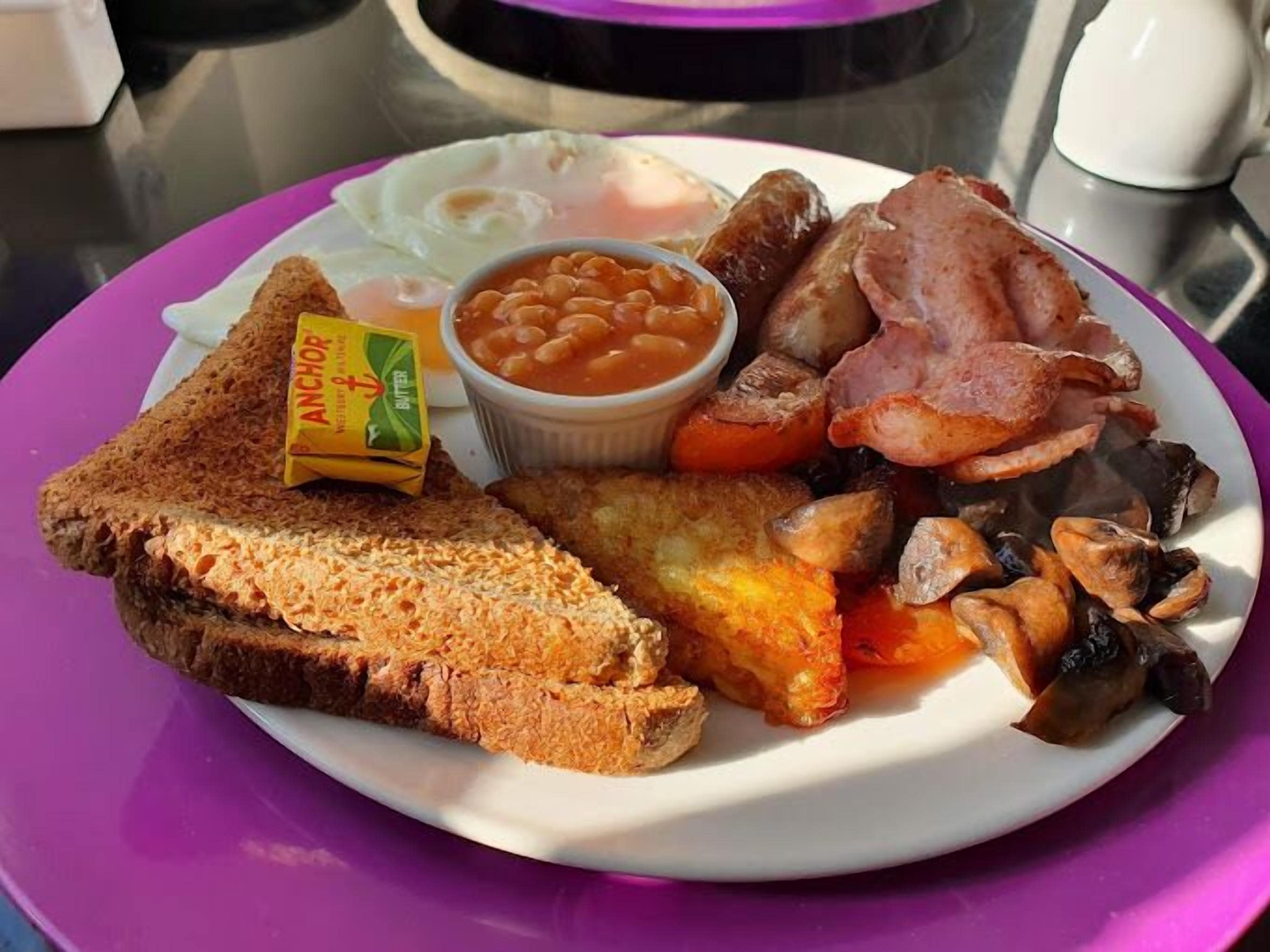 A plate of breakfast food including toast, eggs, beans, sausages, bacon, and mushrooms.