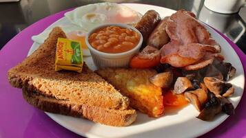 A plate of breakfast food including toast, eggs, beans, sausages, bacon, and mushrooms.