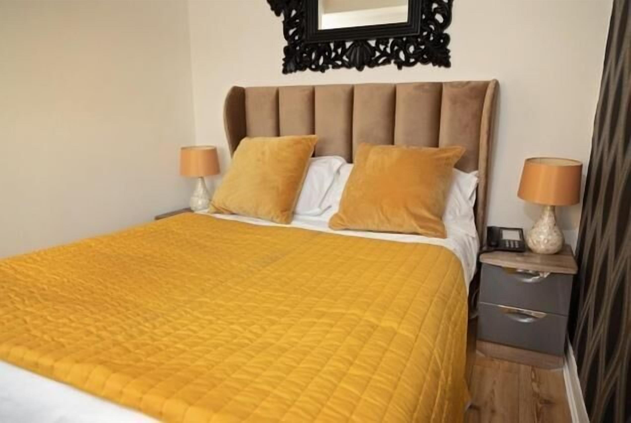 A neatly made bed with a yellow quilt, a brown upholstered headboard, and two bedside lamps.