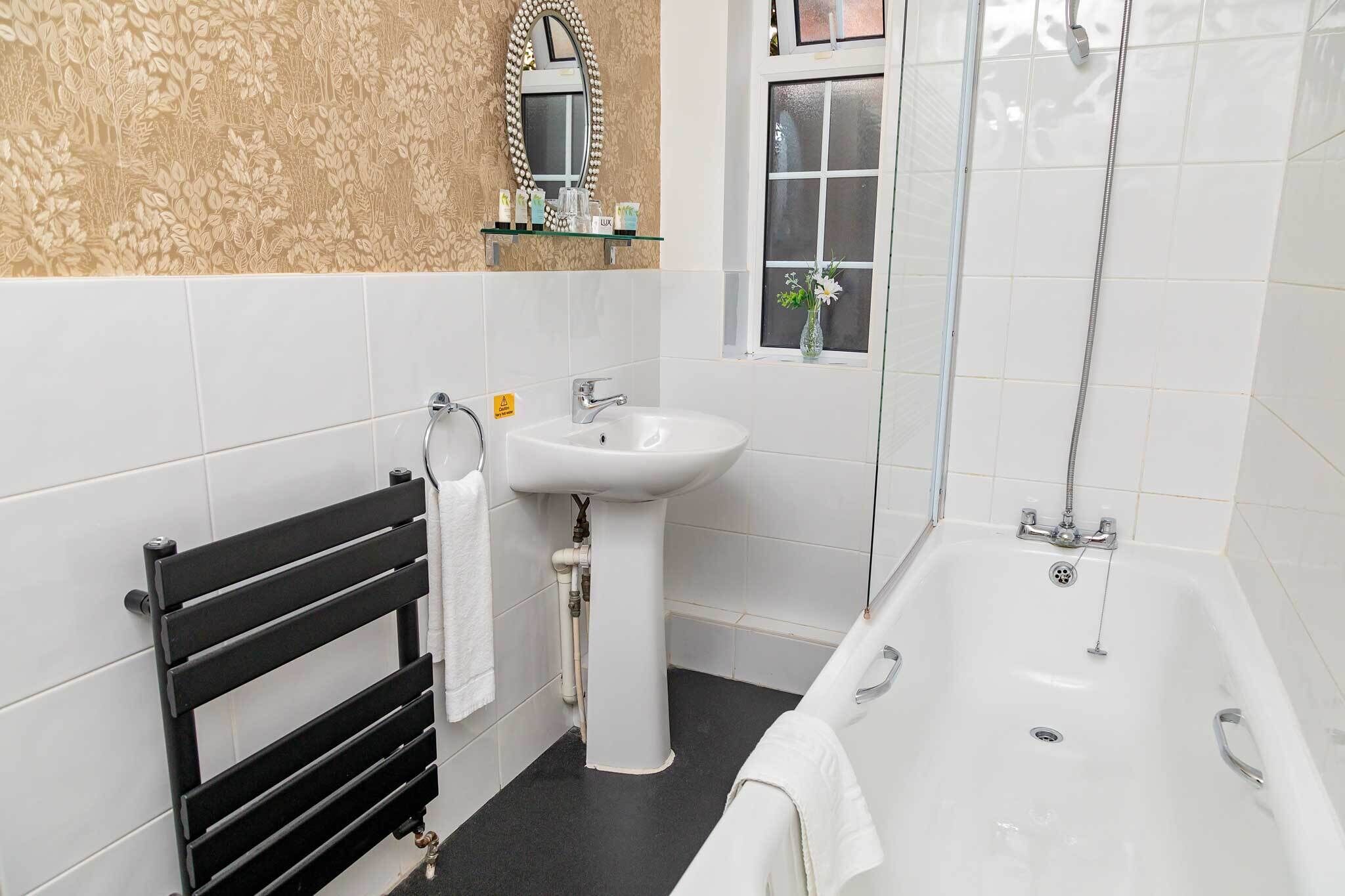 A bathroom with a black towel rack, a white sink, a bathtub, and a window with a view.
