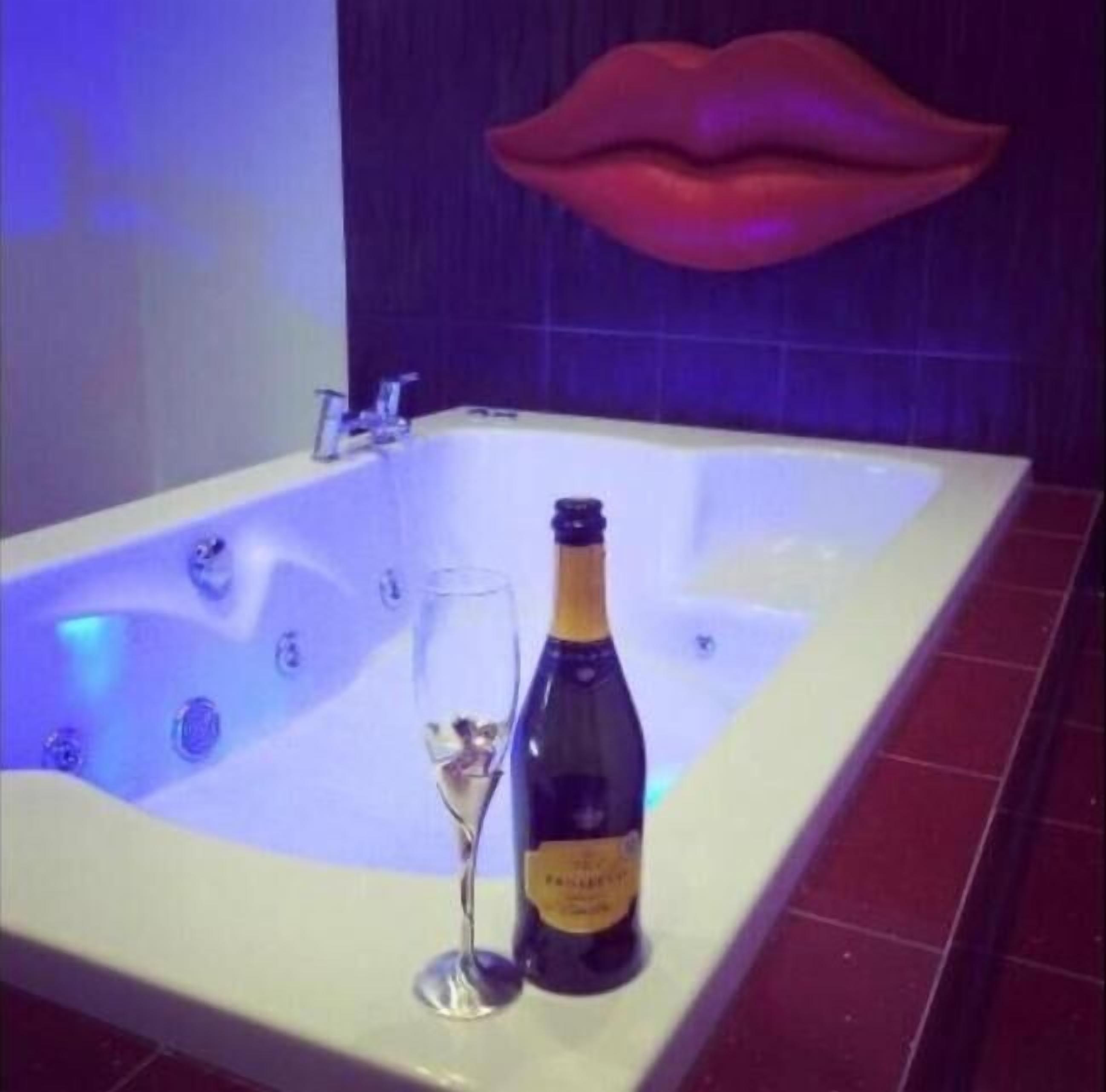 A bathtub with a bottle of champagne and a glass.