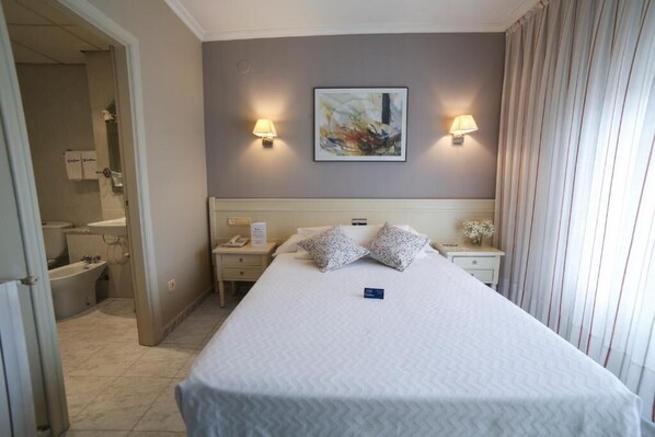 A hotel room with a large bed, two bedside tables, a nightstand, a wall-mounted lamp, and a painting. - San Marcos (Cambados)