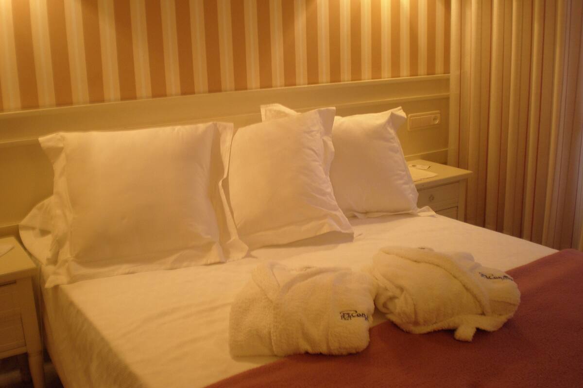A hotel room with a neatly made bed, white pillows, and two towels on the bed.