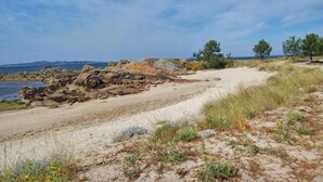 A coastal landscape with a sandy beach, rocky outcrops, and sparse vegetation. - San Marcos (Cambados)