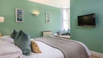 Een slaapkamer met een bed, twee kussens, een deken, een flatscreen televisie en twee ingelijste foto's aan de muur.