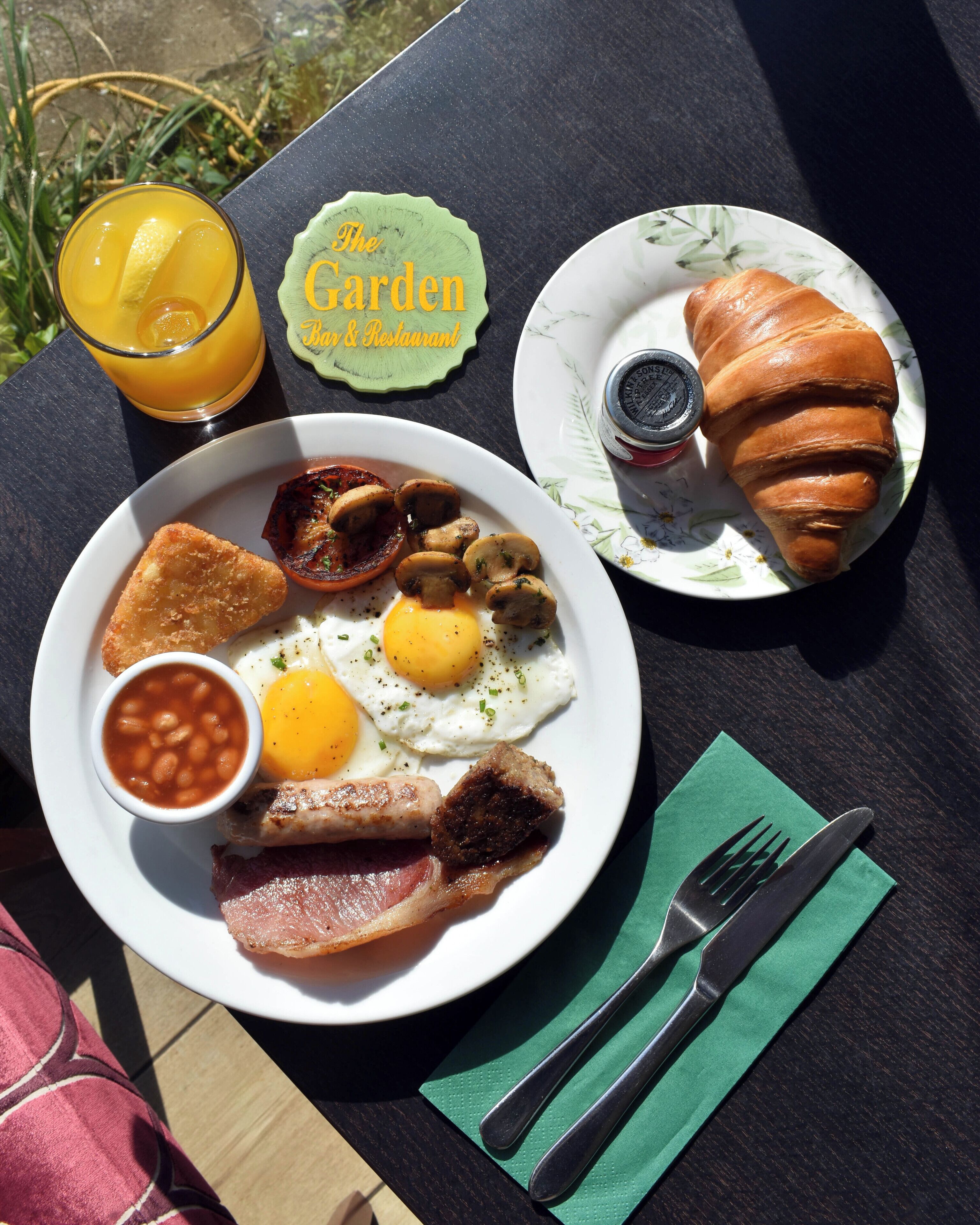 A breakfast plate with eggs, bacon, mushrooms, and beans, a croissant, and a glass of orange juice on a table.