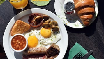 A breakfast plate with eggs, bacon, mushrooms, and beans, a croissant, and a glass of orange juice on a table.