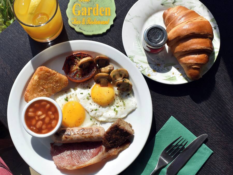 A breakfast plate with eggs, bacon, mushrooms, and beans, a croissant, and a glass of orange juice on a table.
