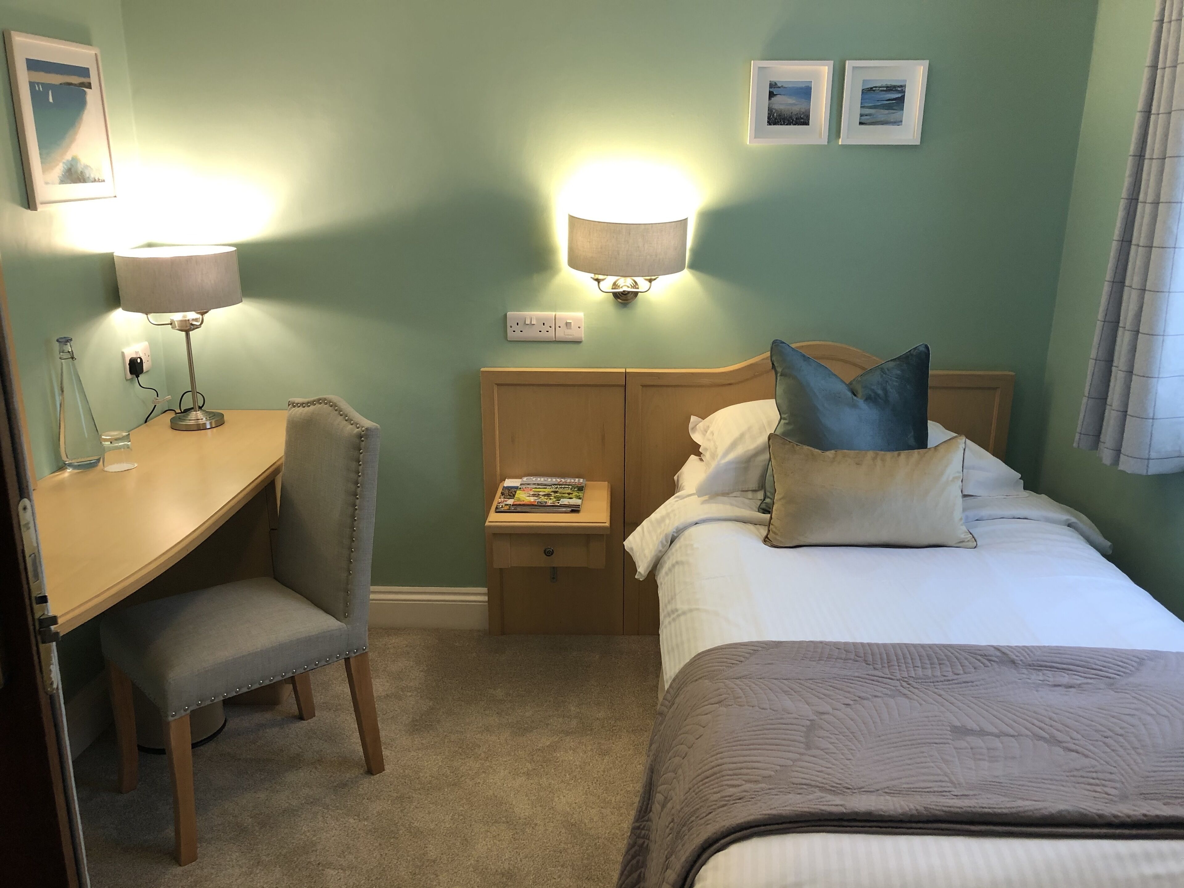 A hotel room with a bed, a desk, a chair, and two wall-mounted lamps.