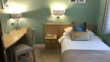 A hotel room with a bed, a desk, a chair, and two wall-mounted lamps.