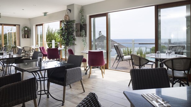 A restaurant with outdoor seating, large windows, and a view of the sea. - Hotel Penzance Harbour View (Penzance)