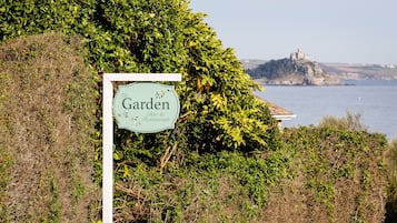 A sign for 'The Garden Bar & Restaurant' with a view of a castle on a cliff by the sea.