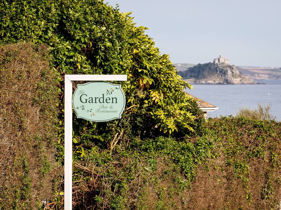 A sign for 'The Garden Bar & Restaurant' with a view of a castle on a cliff by the sea.