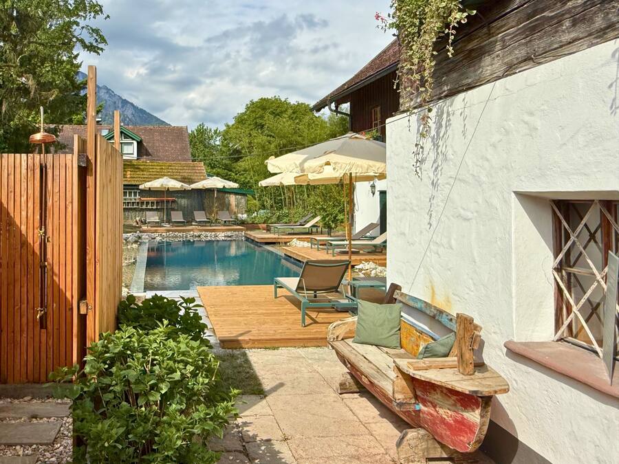 Ein Poolbereich mit Liegestühlen und Sonnenschirmen, ein hölzernes Boot und ein weißes Gebäude mit einem Fenster.