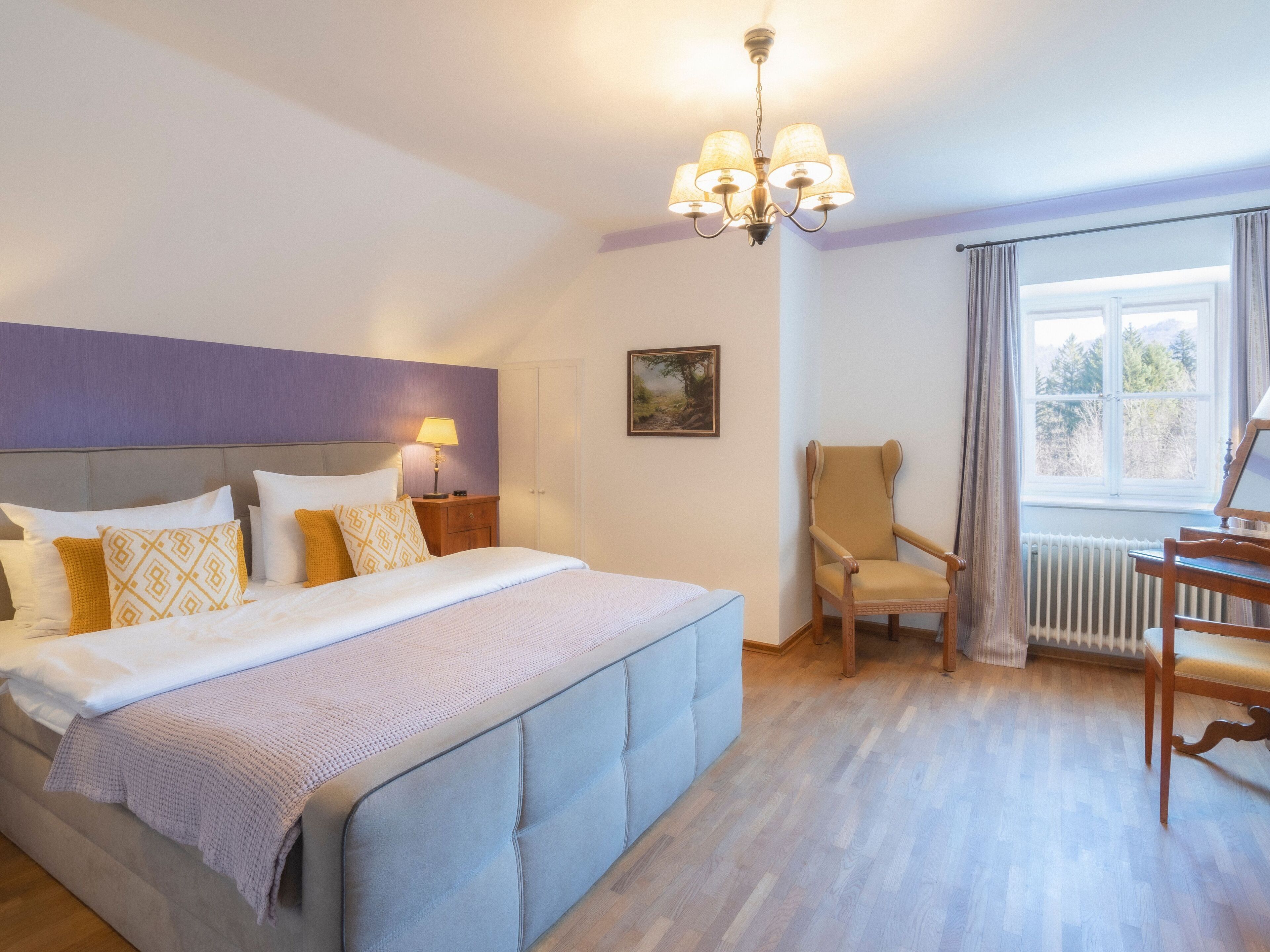 A bedroom with a large bed, a chair, a desk, and a window with curtains.