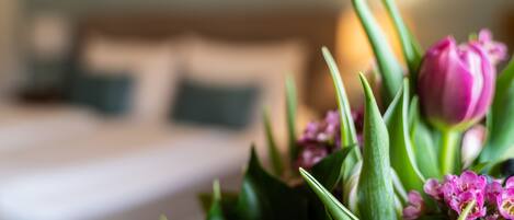 Un ramo de flores con hojas verdes y delicadas flores rosadas en una habitación con fondo desenfocado.