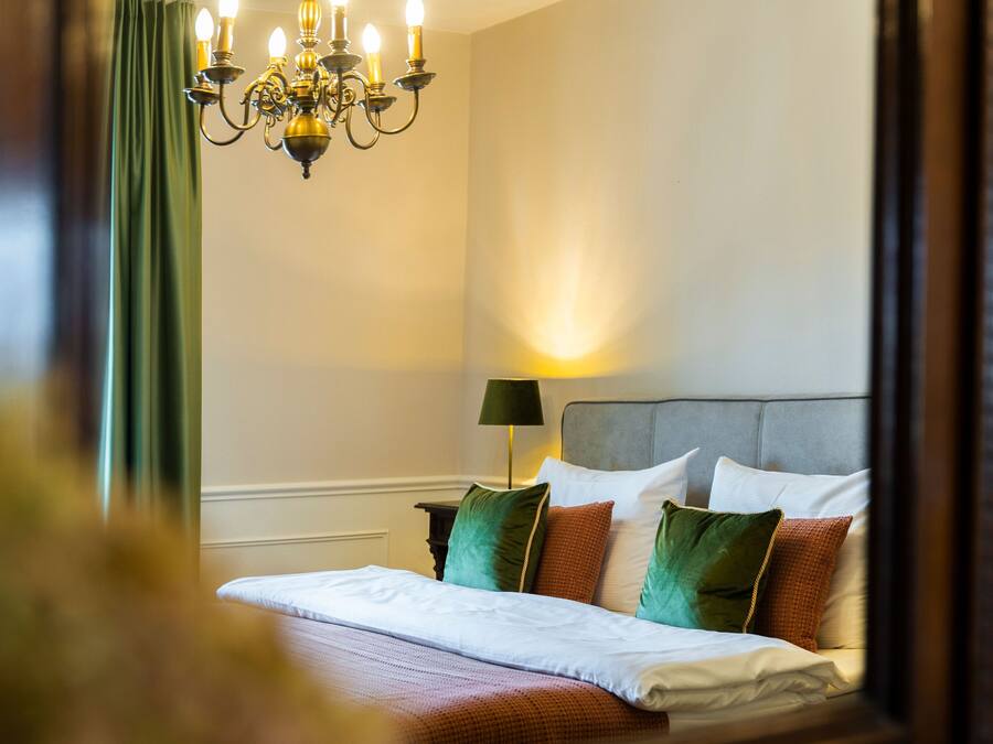 A hotel room with a bed, a nightstand, a lamp, and a chandelier.