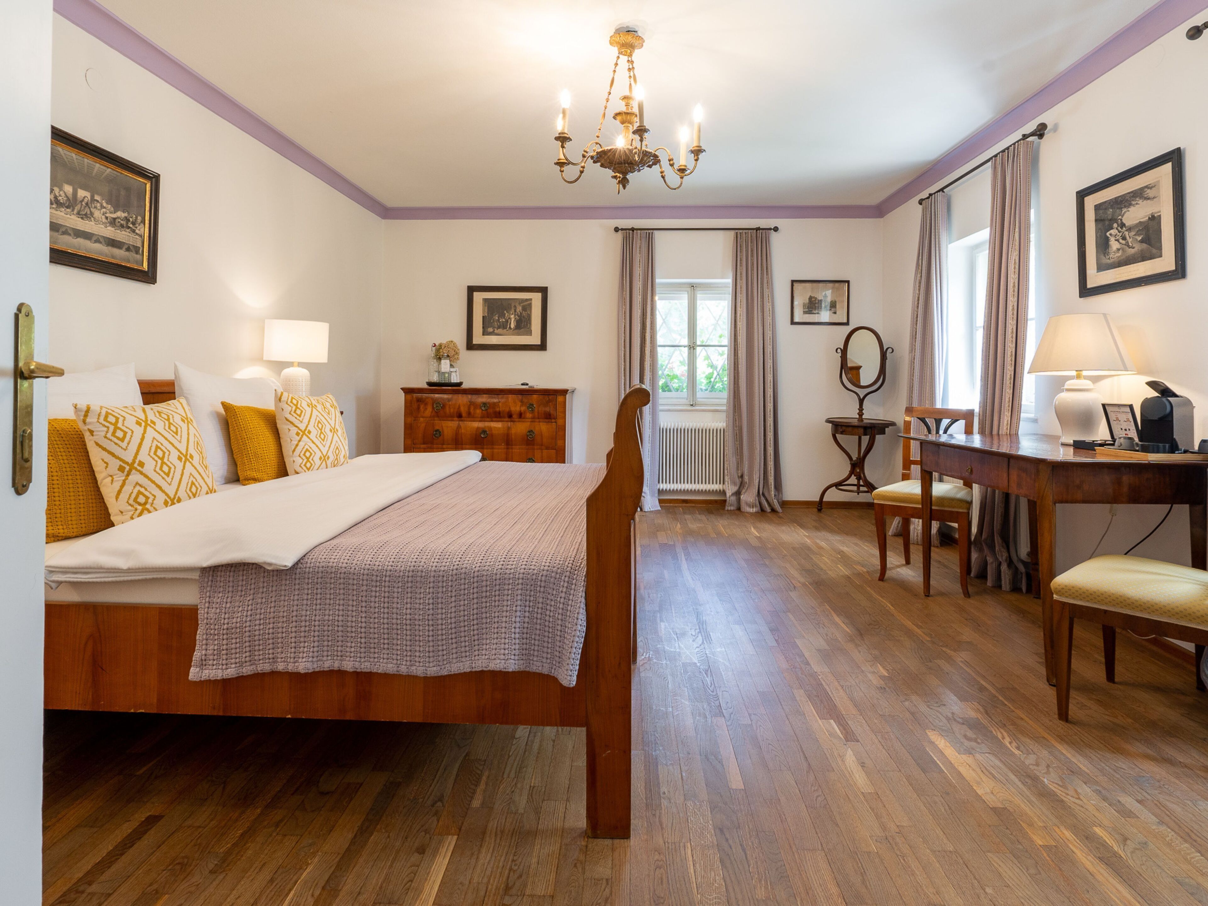 A bedroom with a wooden bed, a desk with a chair, a dresser, and a window with curtains.