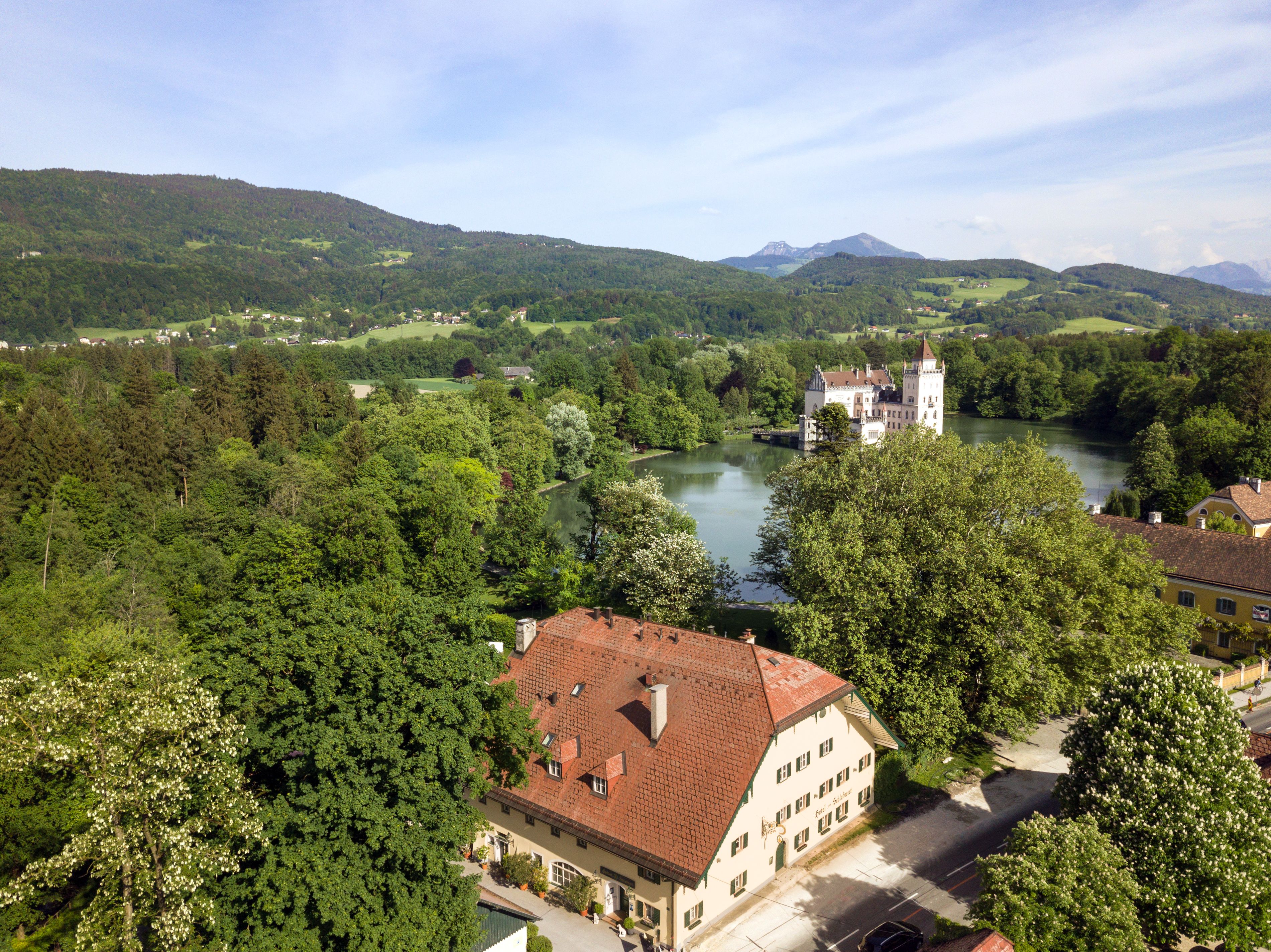 Ein schlösserähnliches Gebäude mit rotem Ziegeldach, umgeben von üppigem Grün und einem Fluss.