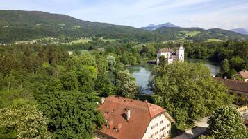 Ein schlösserähnliches Gebäude mit rotem Ziegeldach, umgeben von üppigem Grün und einem Fluss.