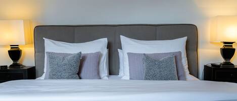 A neatly made bed with a grey headboard and two bedside tables with lamps.