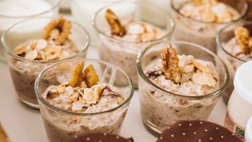 Uma série de pequenas tigelas de vidro repletas de uma sobremesa cremosa, coberta com frutos secos e fruta desidratada.