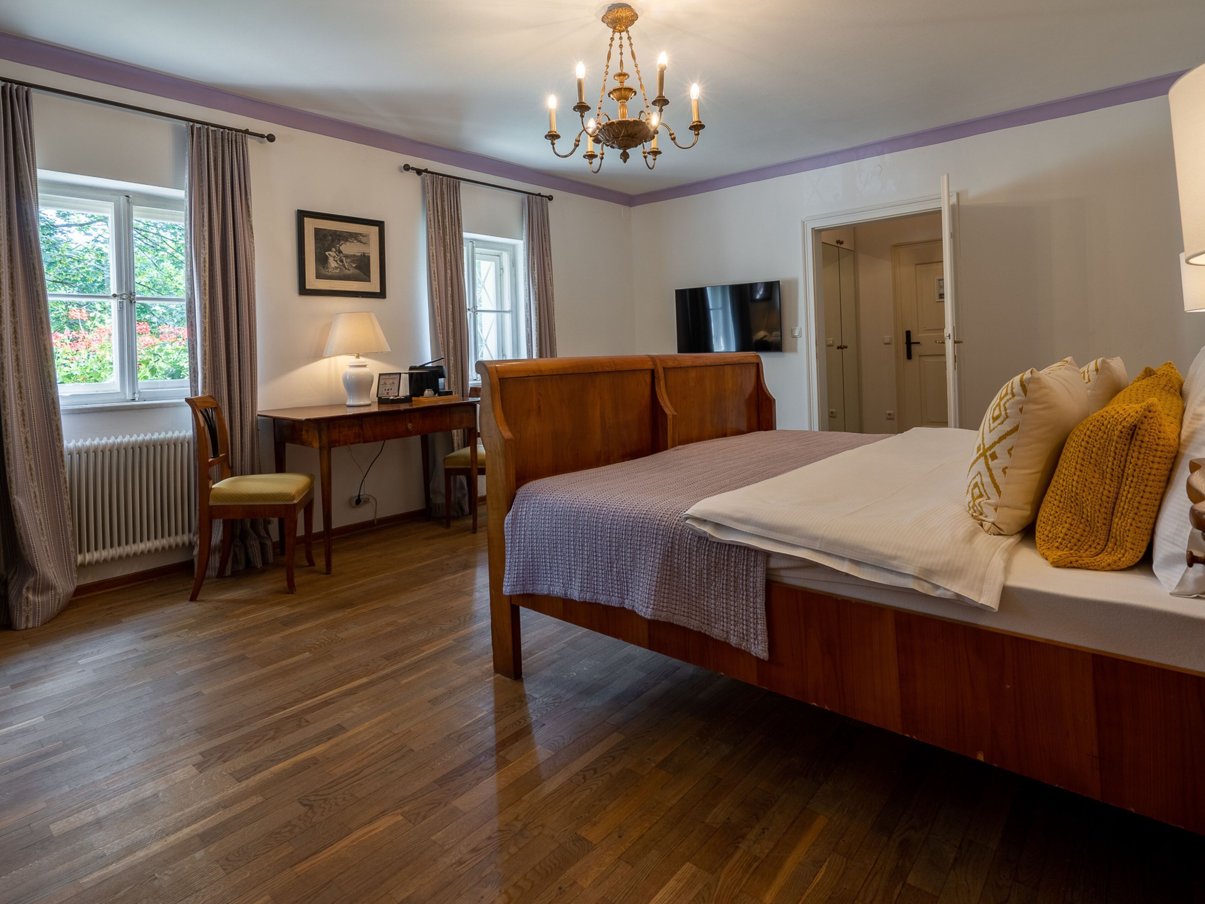 A bedroom with a wooden bed, a desk with a chair, a radiator, and a window with curtains.