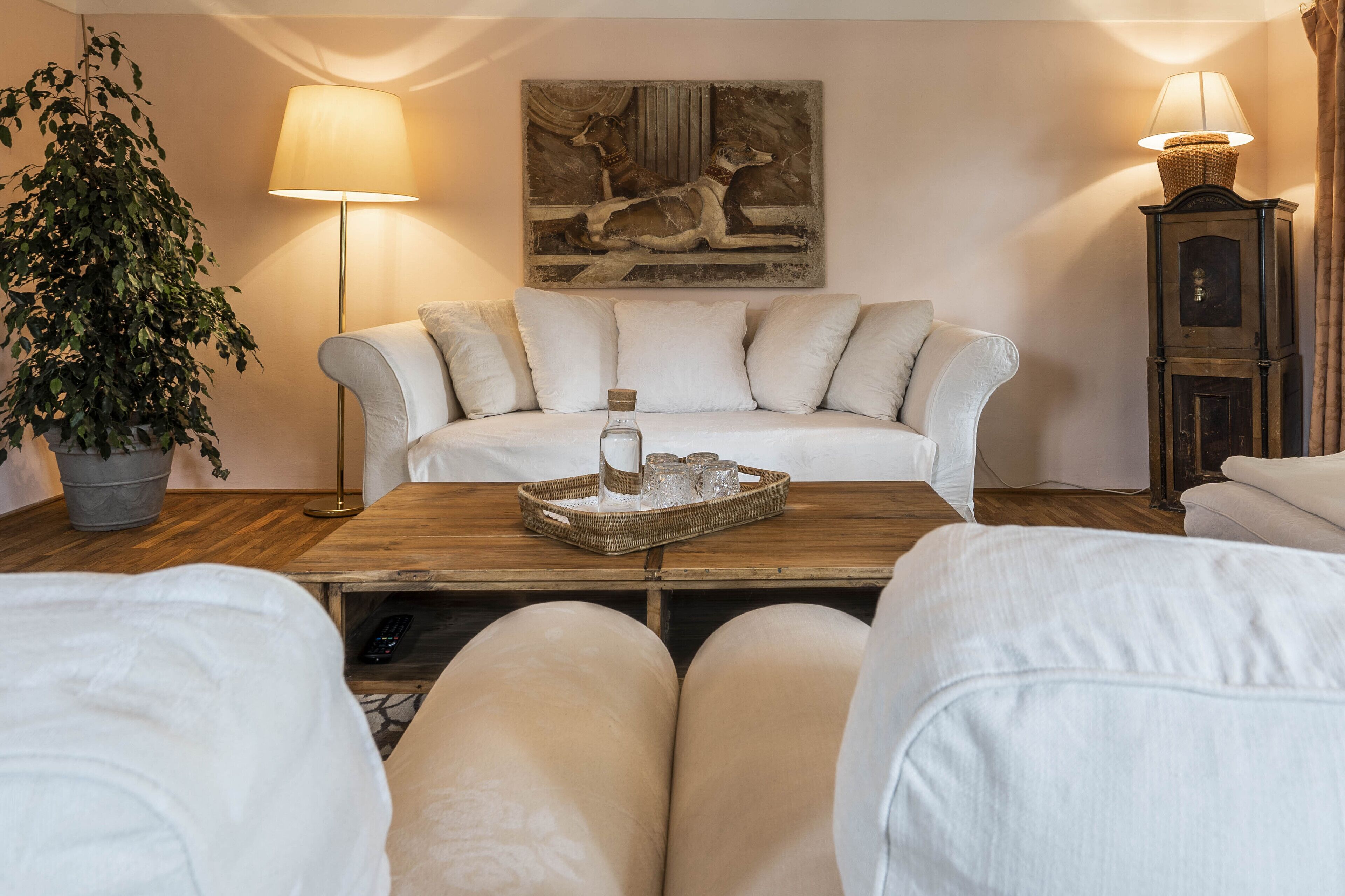 Ein Wohnzimmer mit einer Couch, einem Couchtisch mit Tablett, einer Lampe und einem Gemälde an der Wand.
