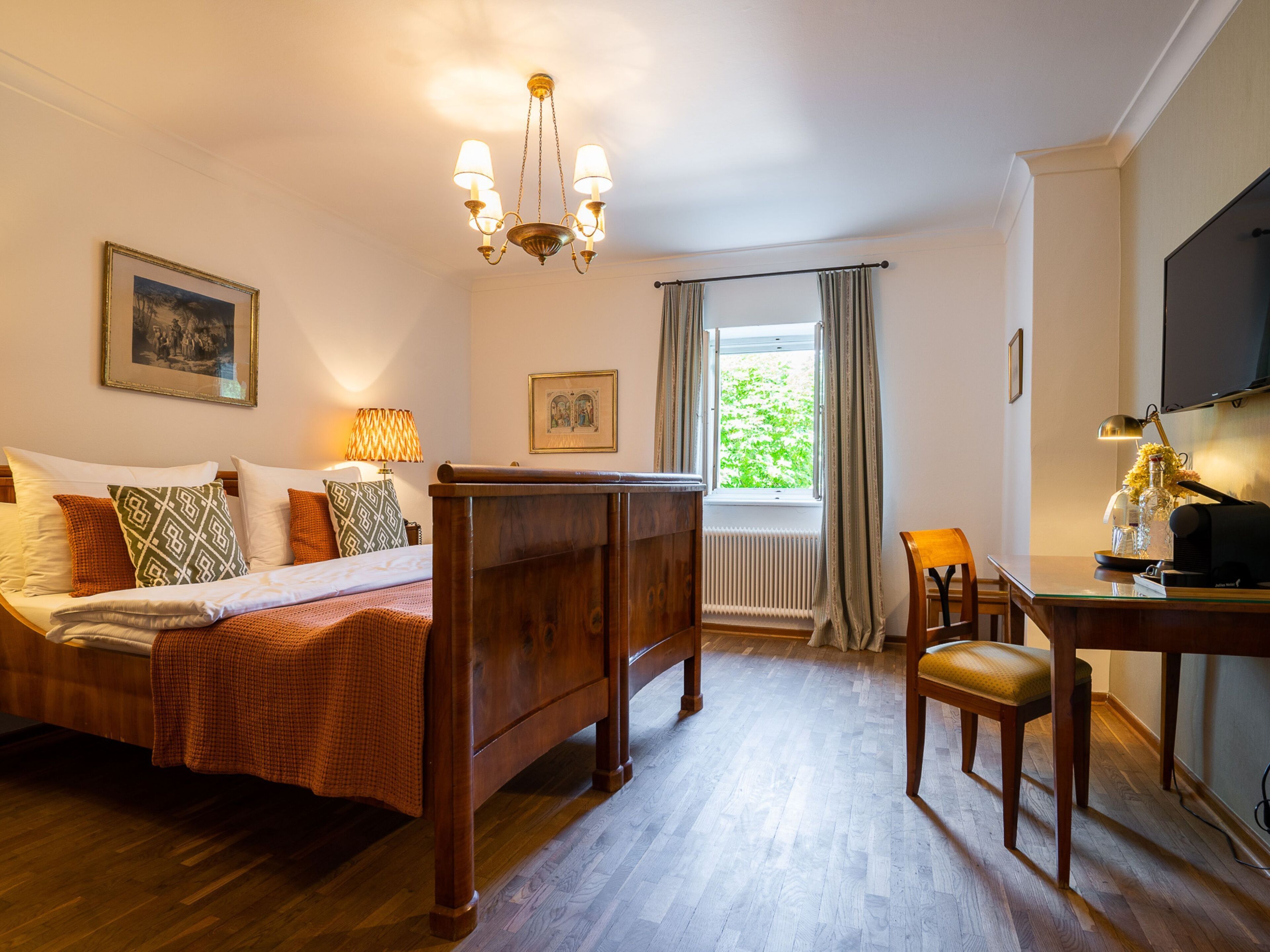 A hotel room with a wooden bed, a desk with a chair, a television, and a window with curtains.