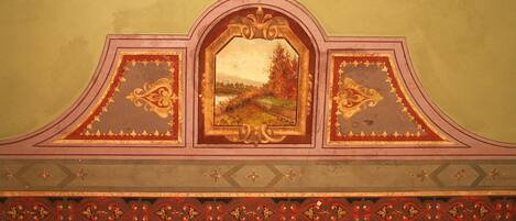 Un techo decorativo con un cuadro de paisaje enmarcado en el centro, diseños ornamentales dorados y rojos, y un diseño simétrico.