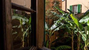 Une fenêtre donnant sur un bâtiment et un jardin où l’on peut voir des bananiers.