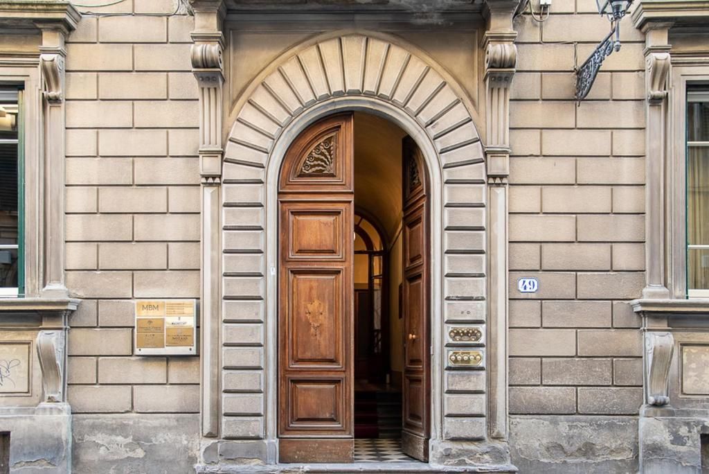 A building entrance with a large wooden door, an arched doorway, and a brick facade.