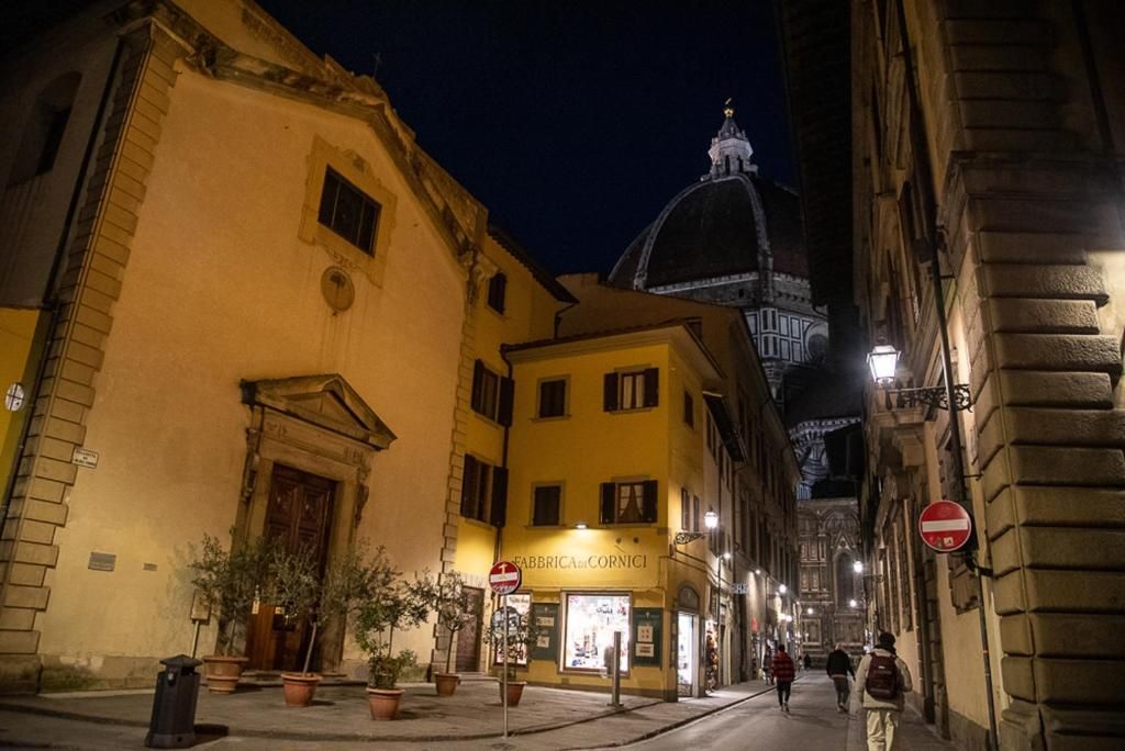 Una calle nocturna con edificios, una tienda llamada 'FABBRICA e CORNICI' y una estructura en forma de cúpula al fondo.