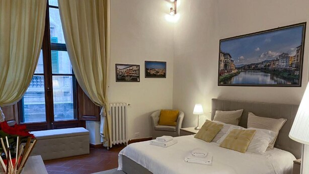 Ein Hotelzimmer mit einem großen Bett, einem Sessel, einem Schreibtisch und einem Fenster mit Vorhängen.