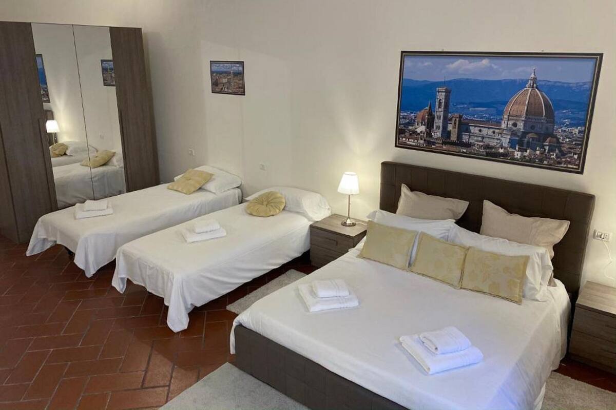 Une chambre d’hôtel avec deux lits simples, un grand miroir, une table de chevet avec une lampe et un tableau représentant un paysage urbain accroché au mur.