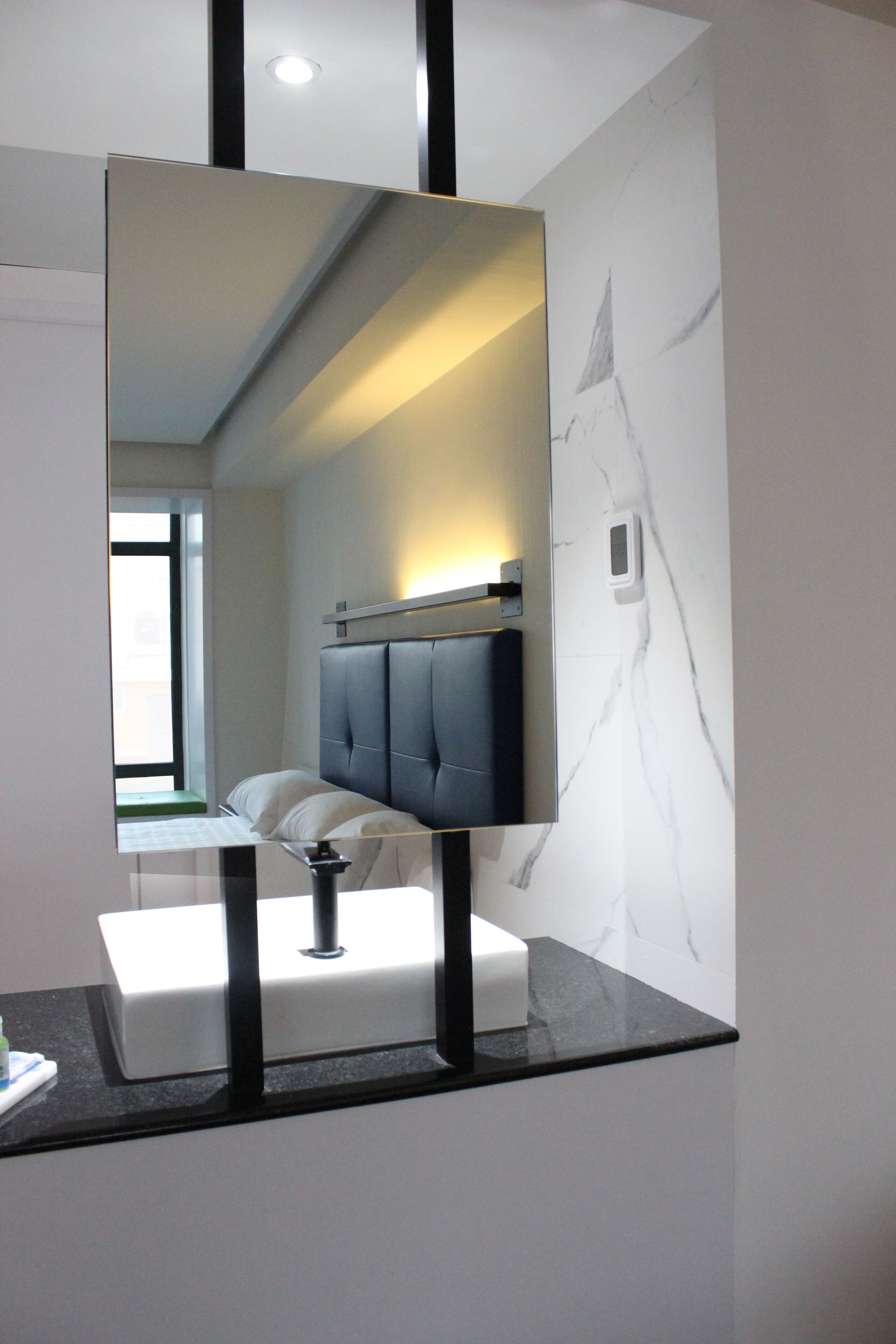 Un baño moderno con un espejo grande, una pared de mármol y una cama con ropa de cama blanca.