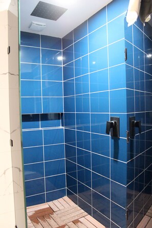 Un baño con paredes de azulejos azules, suelo de madera y cabina de ducha de vidrio.