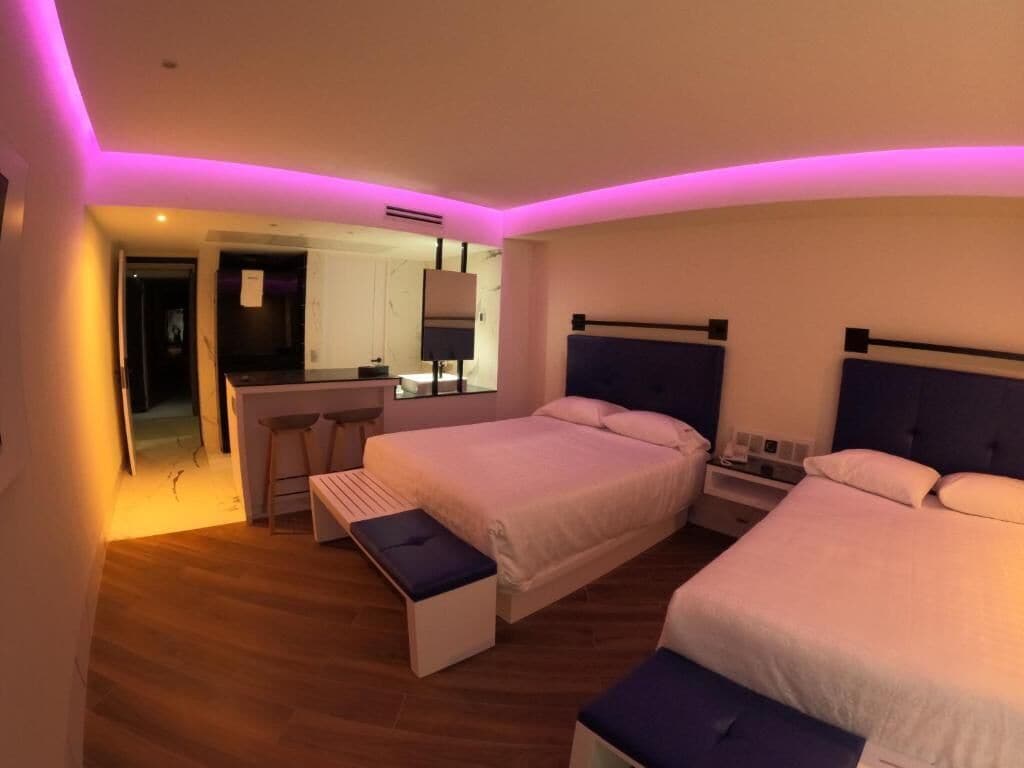 A modern hotel room with two beds, a small desk, and a bench.