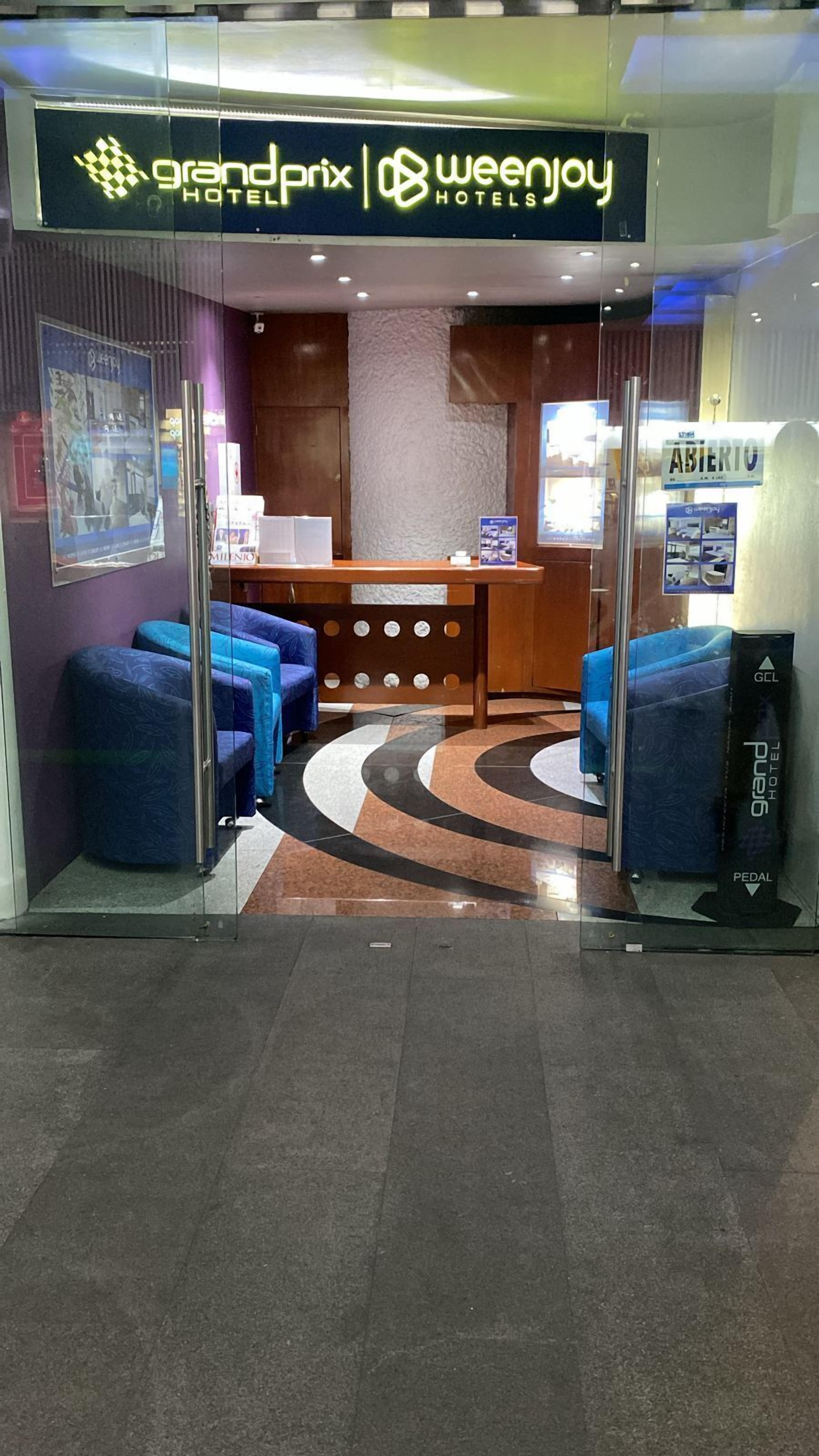 Vestíbulo de hotel con mostrador de recepción, zona de estar azul y suelo estampado.