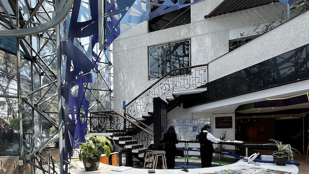 A modern hotel lobby with a circular reception desk, marble flooring, and a staircase leading to upper floors.