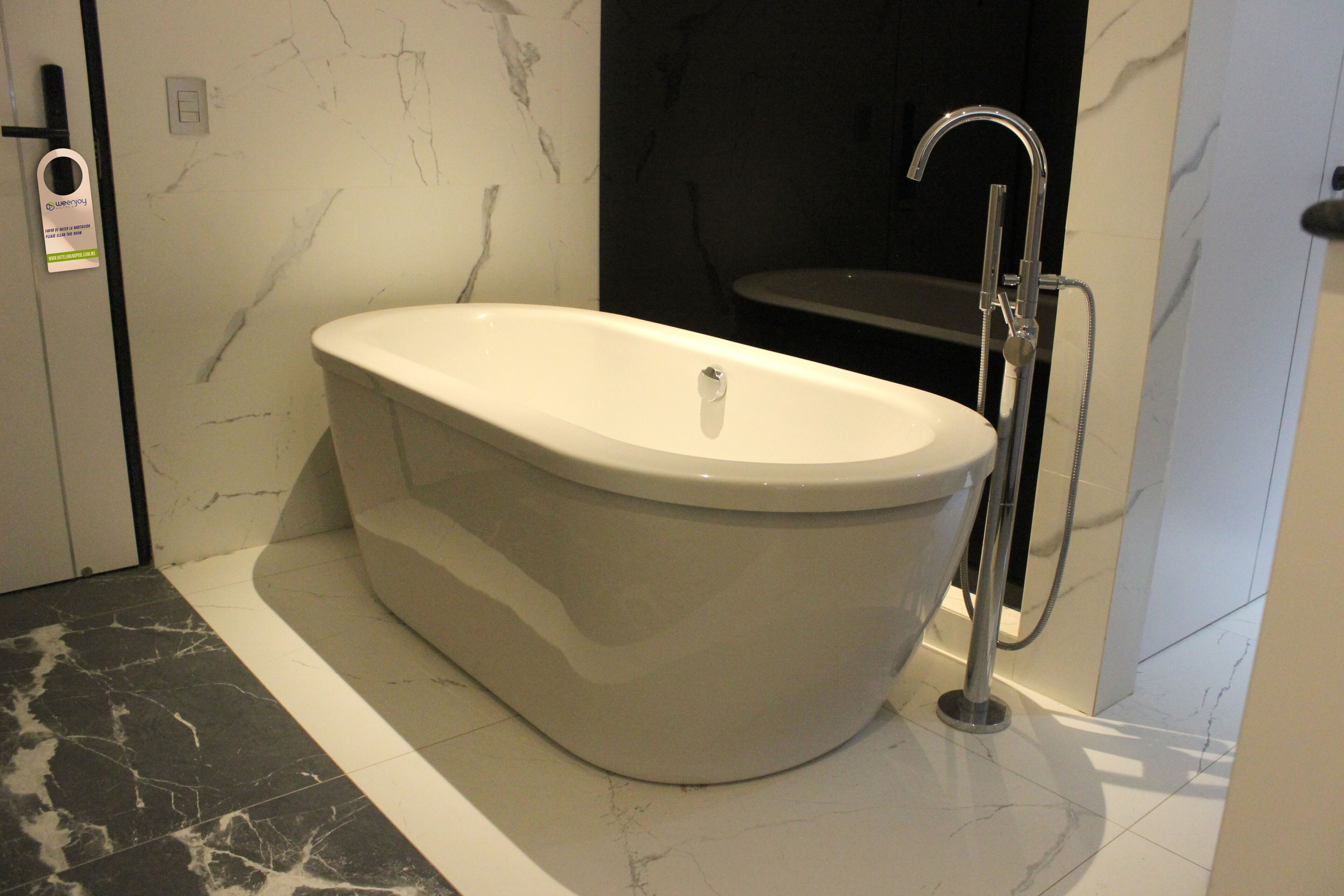 A modern bathroom with a freestanding bathtub, a handheld showerhead, and a marble floor.